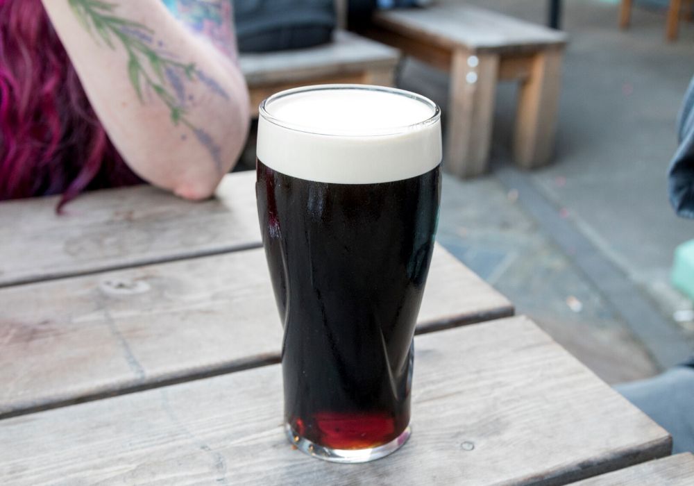 A delicious pint of Guinness beer in a clear glass mug on a wooden table.