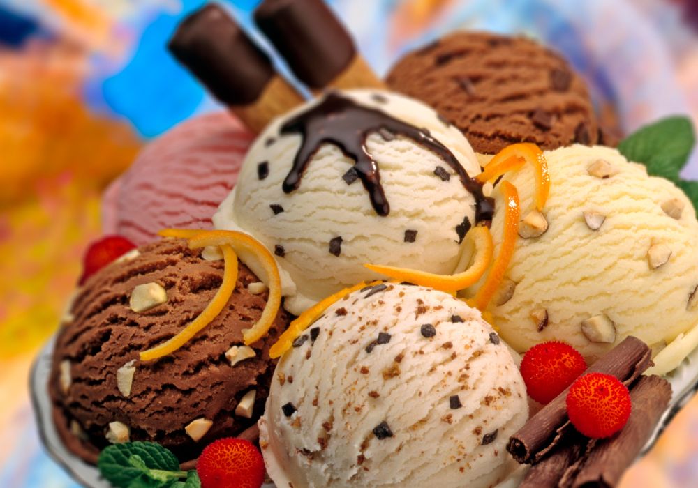 Various flavors of ice cream balls decorated with red fruits, chocolates curls and mint.