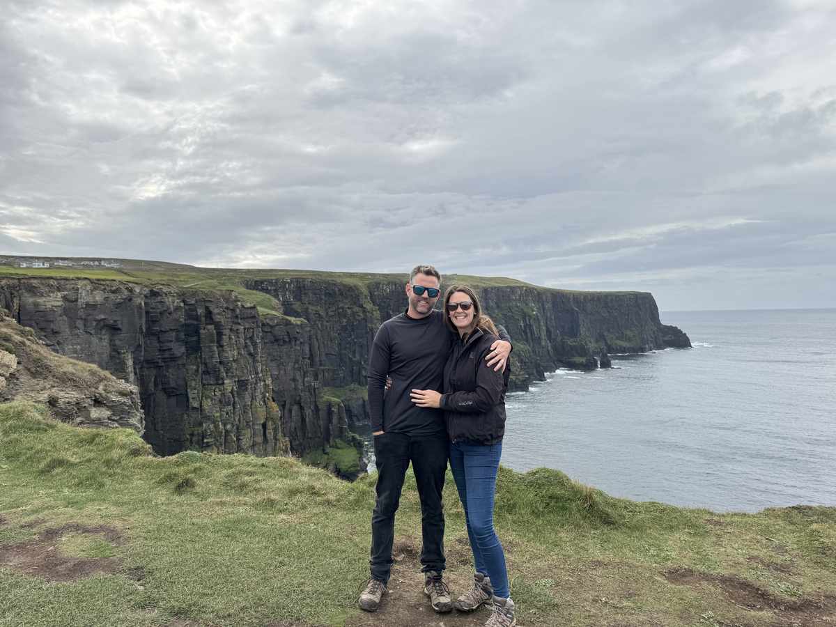 Nick and Dariece standing at the Cliffs of Moher with the coast behind them