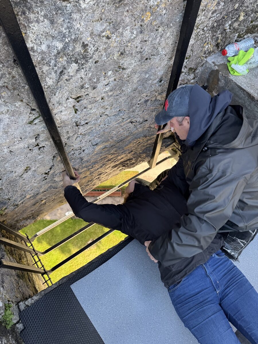 Nick leaning back to kiss the Blarney Stone at the top of Blarney Castle tower