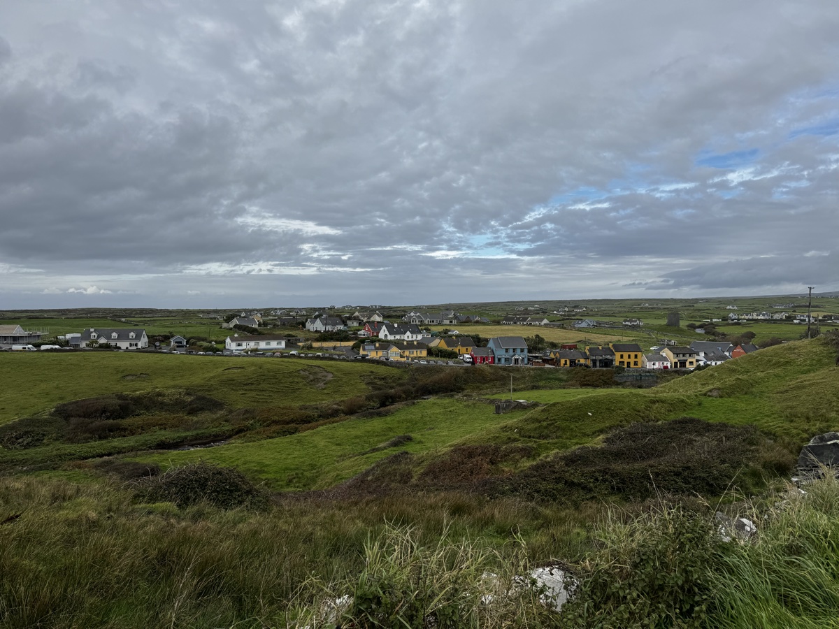 Doolin village viewed from the hillside above with colourful houses and the Atlantic Ocean in the distance