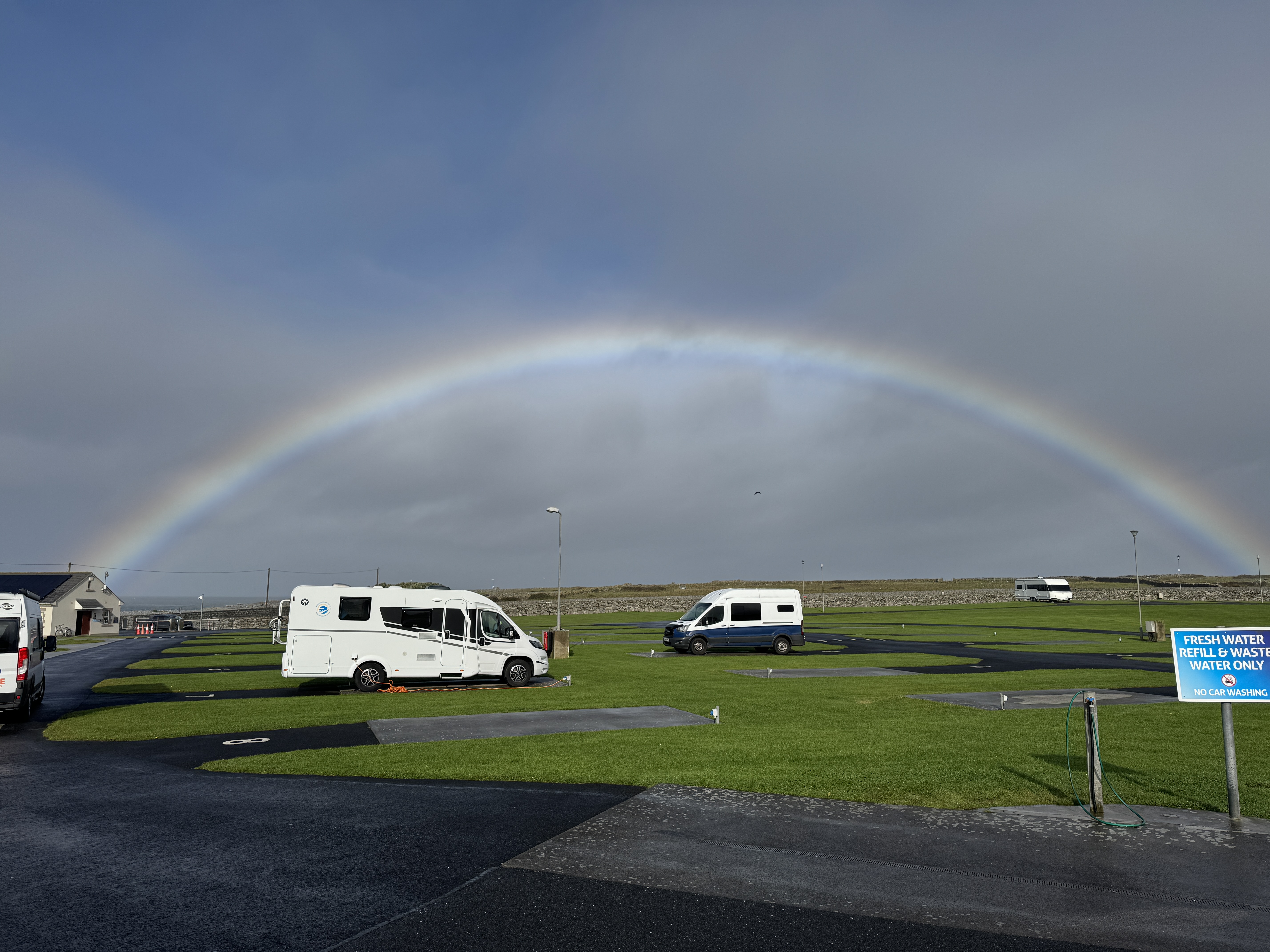 Full rainbow arching over a motorhome campsite in Doolin with campervans parked on green grass