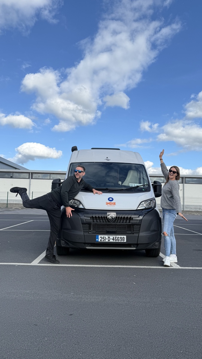 Couple celebrating beside Indie Campers rental campervan in Dublin, Ireland for road trip adventure