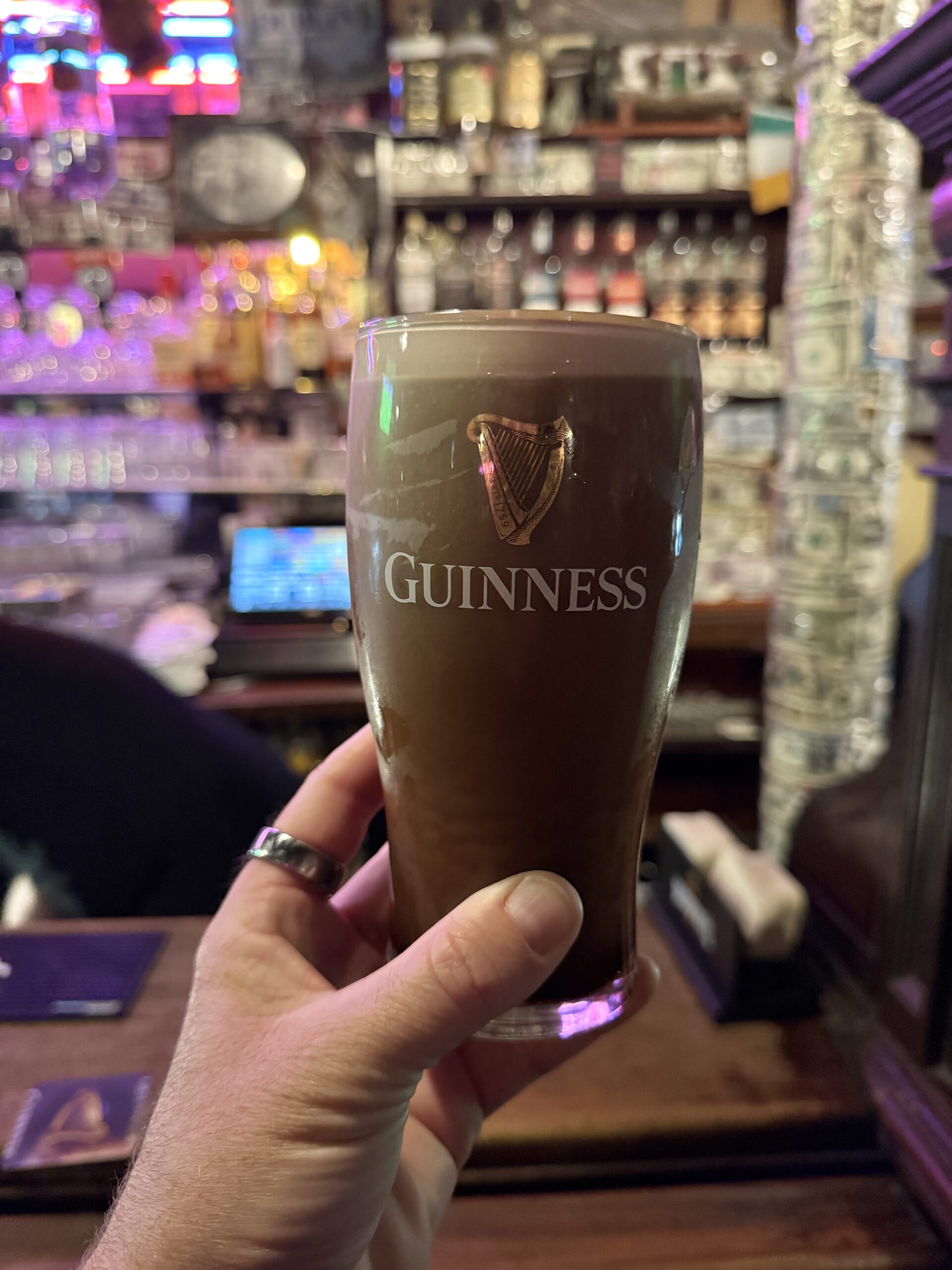 Hand holding a freshly poured settling Guinness pint in a colourful Dublin pub, Ireland