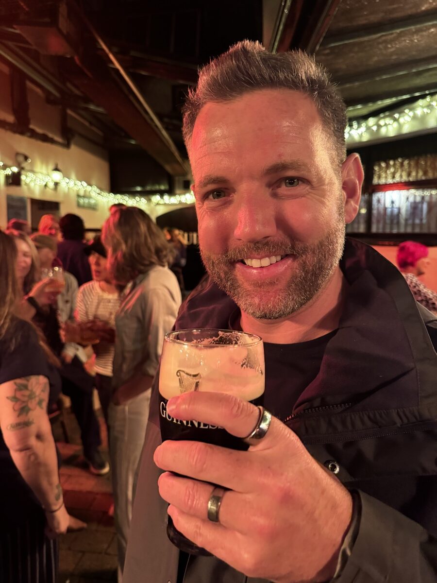 Man smiling with a cocktail in a busy fairy-lit pub in Dublin, Ireland