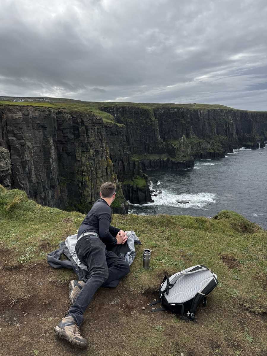 Nick resting on the grassy cliff edge overlooking the Atlantic, Cliffs of Moher, County Clare, Ireland