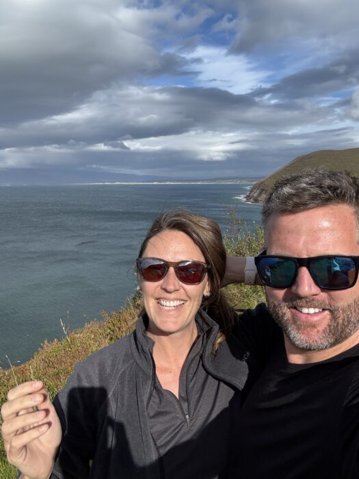 Nick & Dariece smiling on a coastal clifftop with sweeping Ring of Kerry sea views behind, County Kerry, Ireland