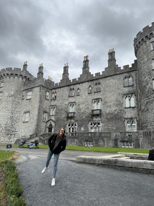 Woman jumping in front of Kilkenny Castle on a cloudy day, County Kilkenny, Ireland