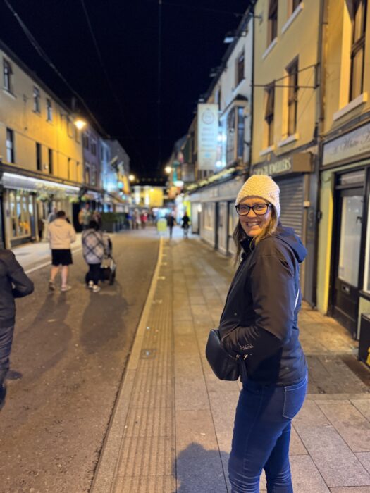 Dariece on the busy main street of Killarney town at night with glowing shopfronts