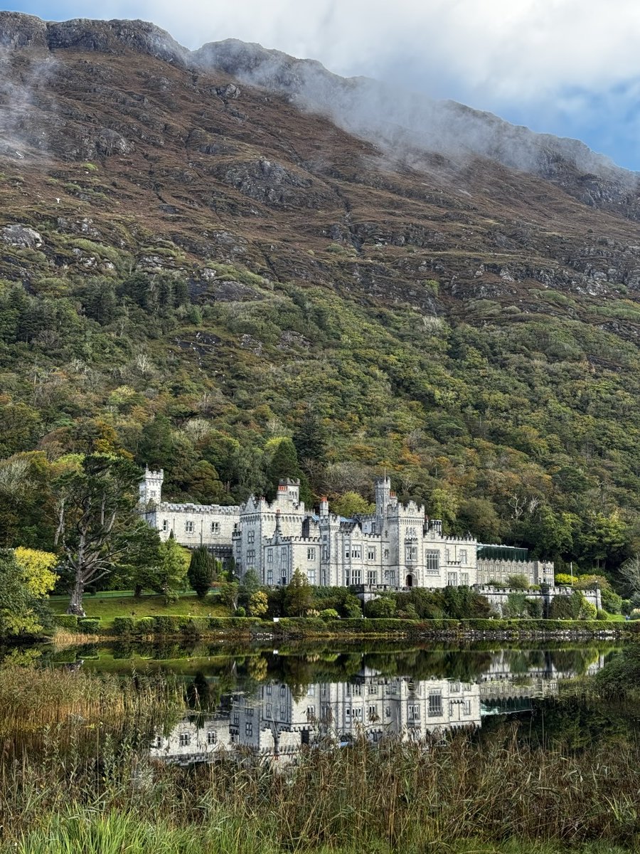 Kylemore Abbey castle reflected in still lake below misty mountain in Connemara, Ireland