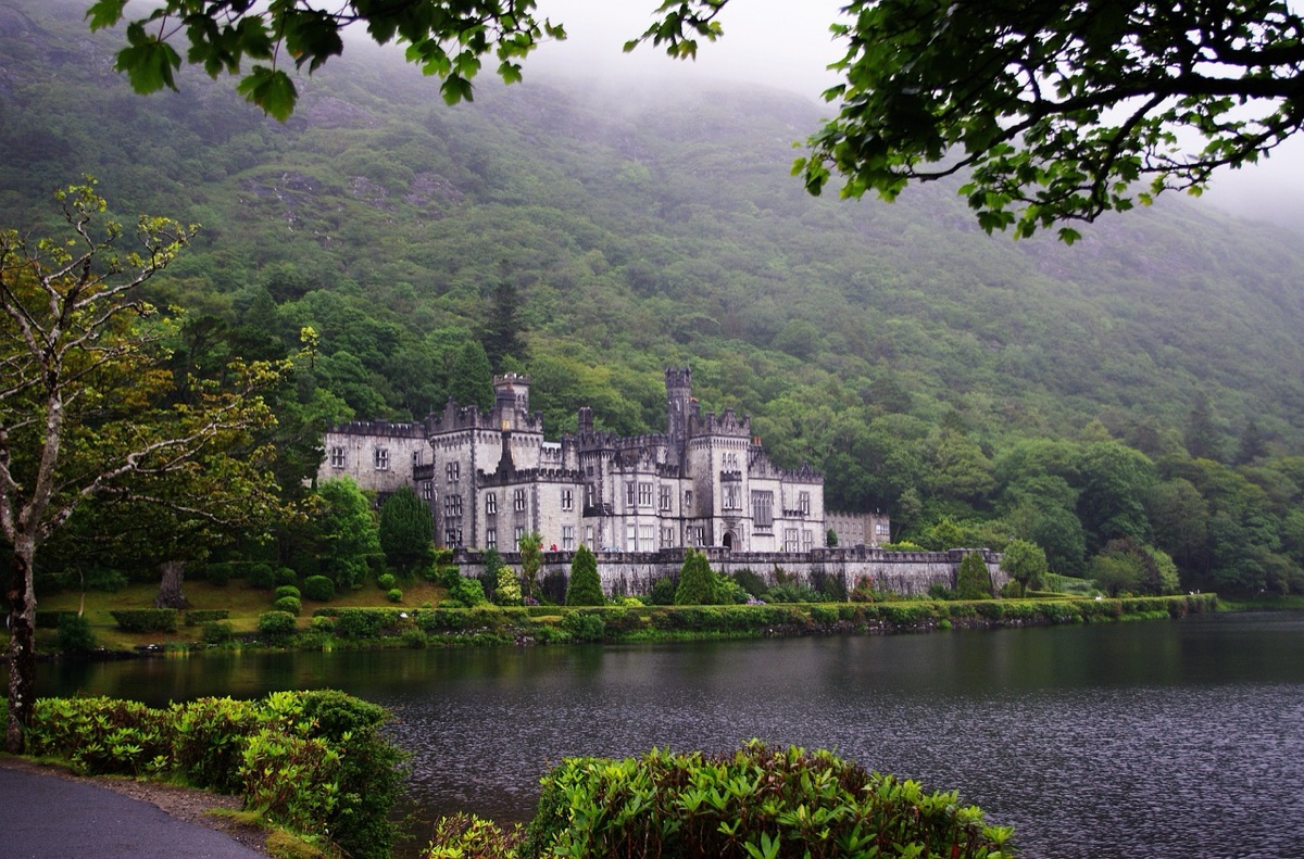gothic castle sits lakeside beneath misty, forested irish hills