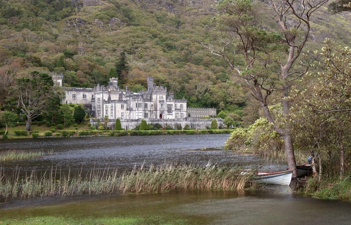 Kylemore Abbey reflected in Pollacapall Lough with a rowing boat moored in the foreground reeds