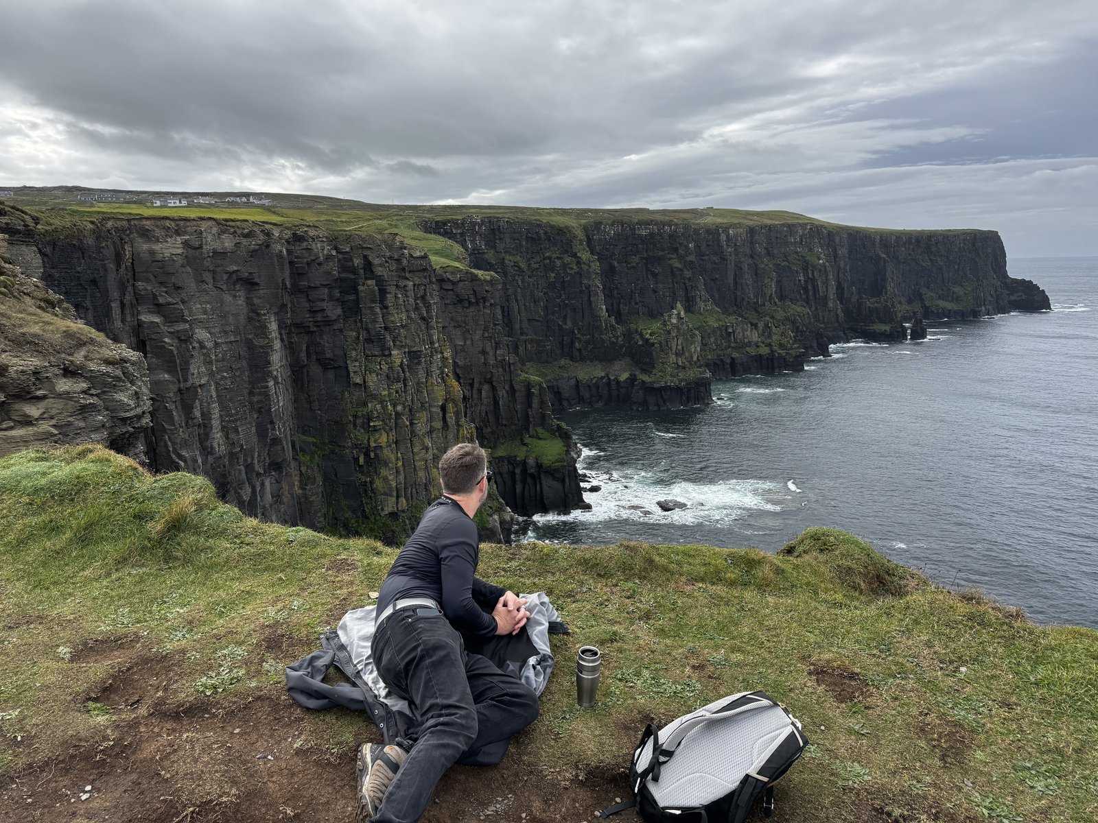 Nick sitting on clifftop overlooking the Cliffs of Moher with sheer cliffs stretching along the Atlantic