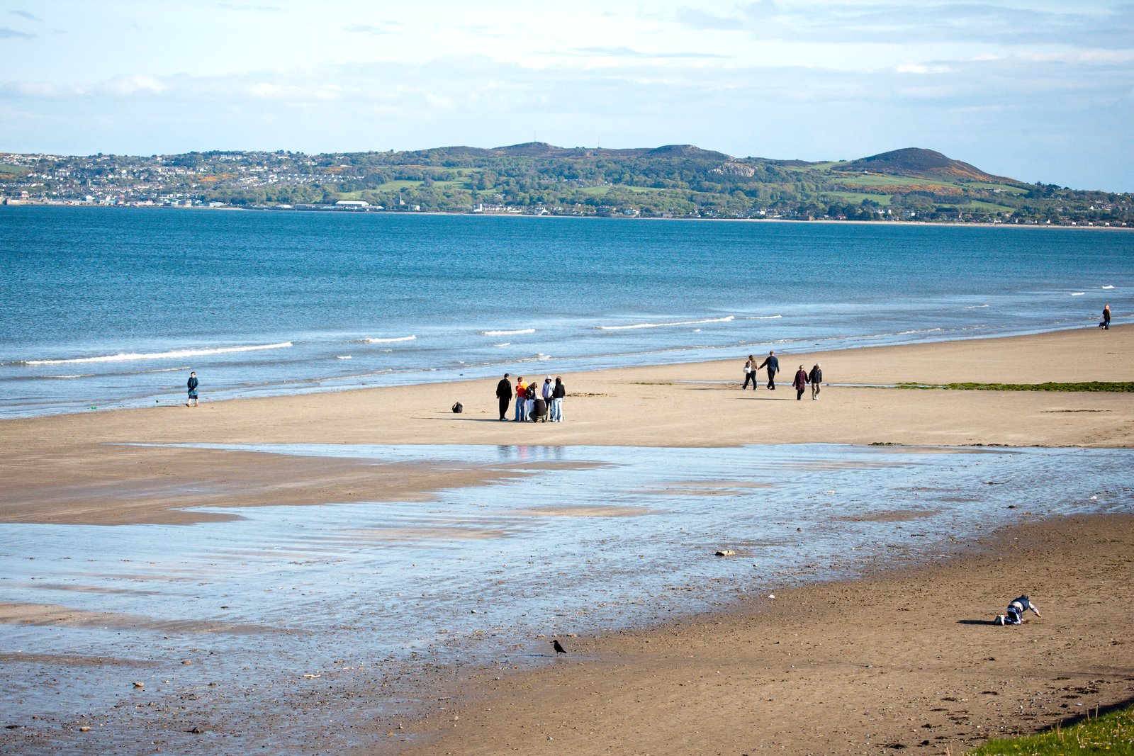 Long flat sandy beach on Dublin Bay with people walking and green hills behind