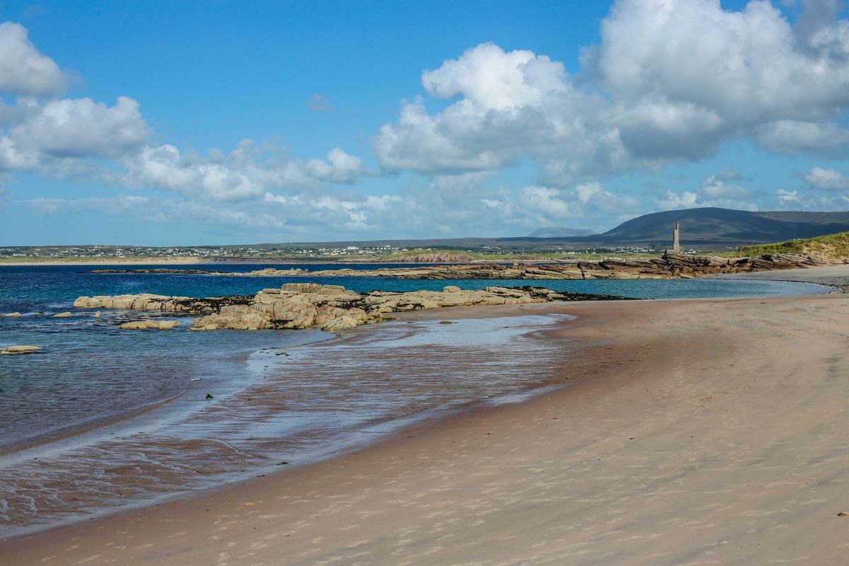 Wide sandy beach at Trá Mór in Rosguill, Donegal, with rocks and a hill behind