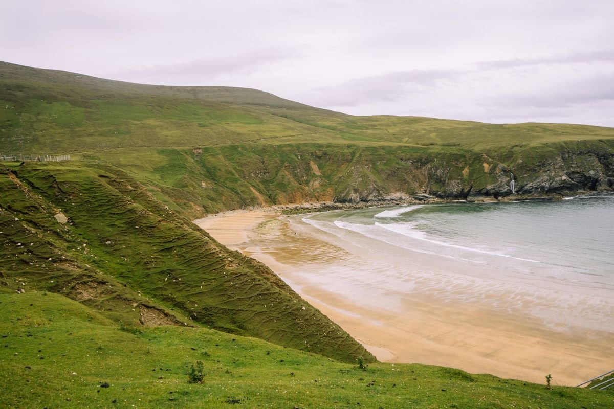 A curved sandy beach tucked between green cliffs at Keem Bay on Achill Island, Mayo.