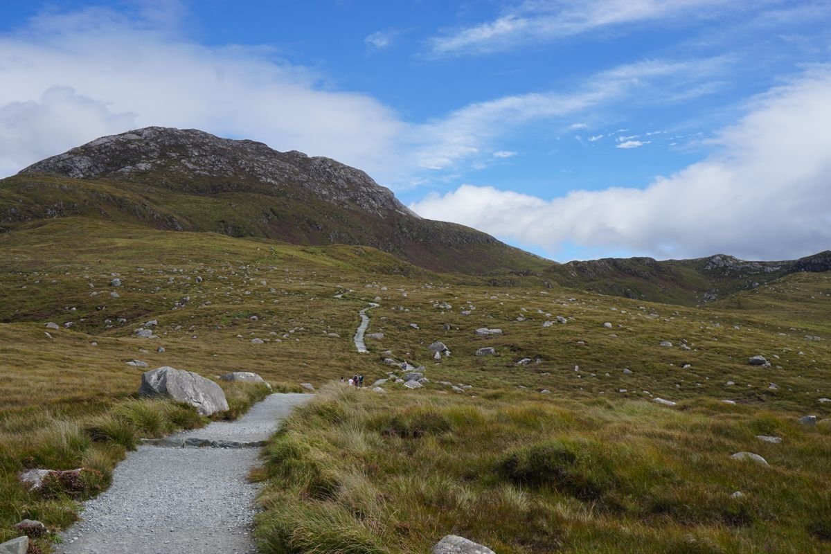 A green mountain and path in Connemara under a bright summer sky