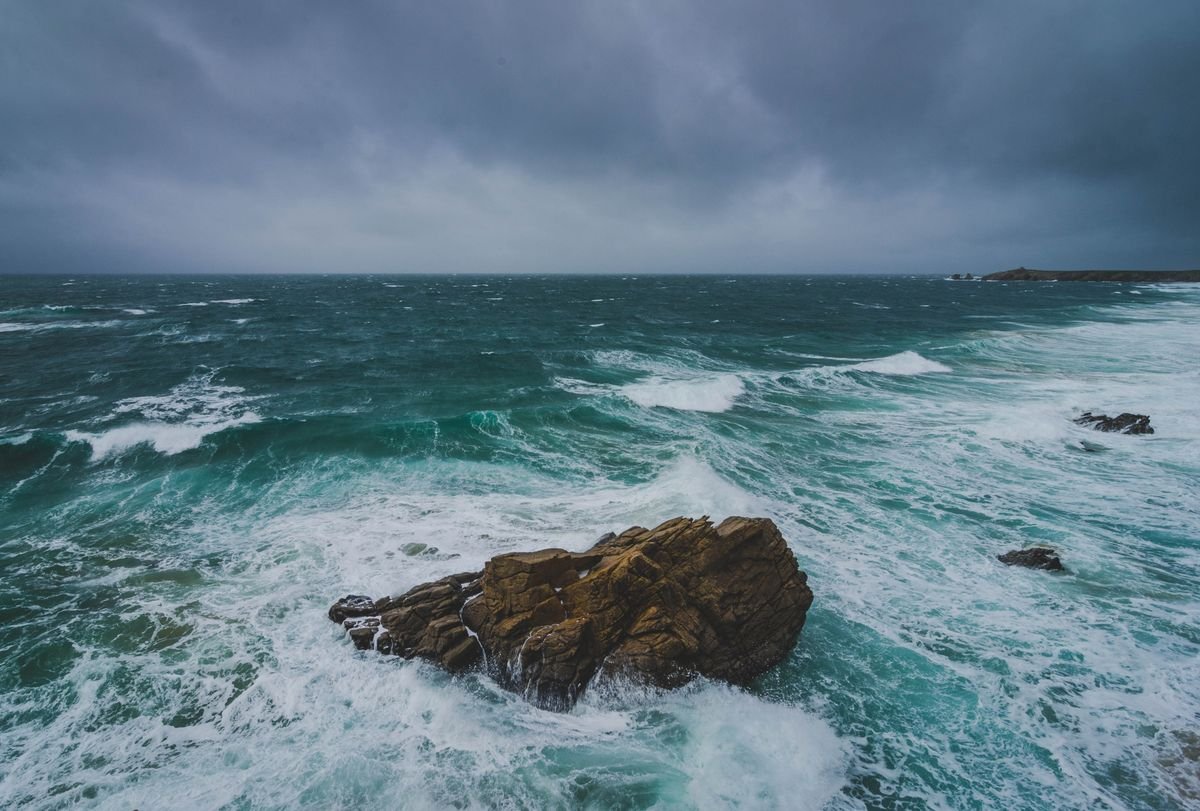 Stormy Atlantic waves breaking over a rock under dark grey clouds