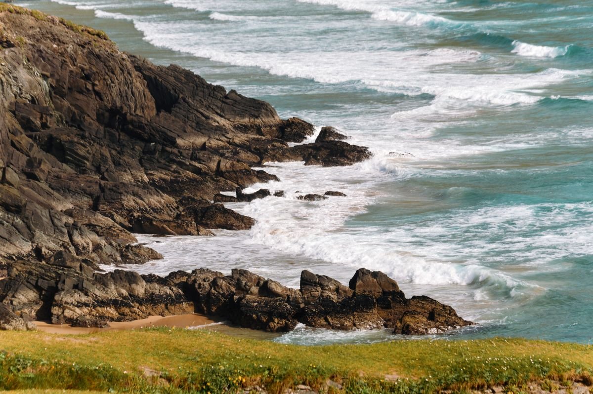 Waves breaking against a rocky Irish shore below a grassy bank