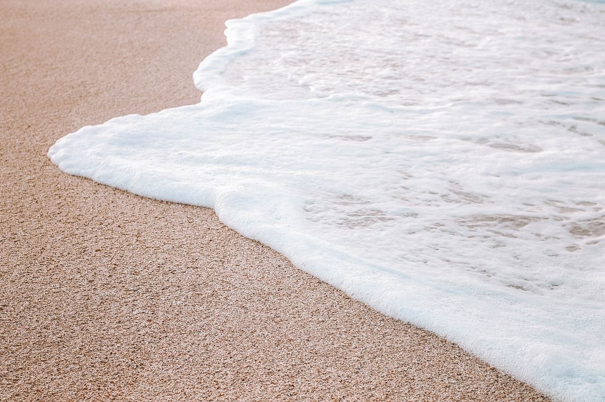 White foam from a wave washing over wet golden sand
