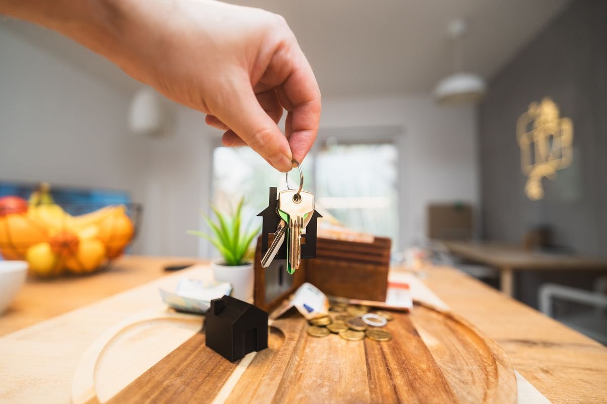 A hand holding a house key with euro coins on a wooden table