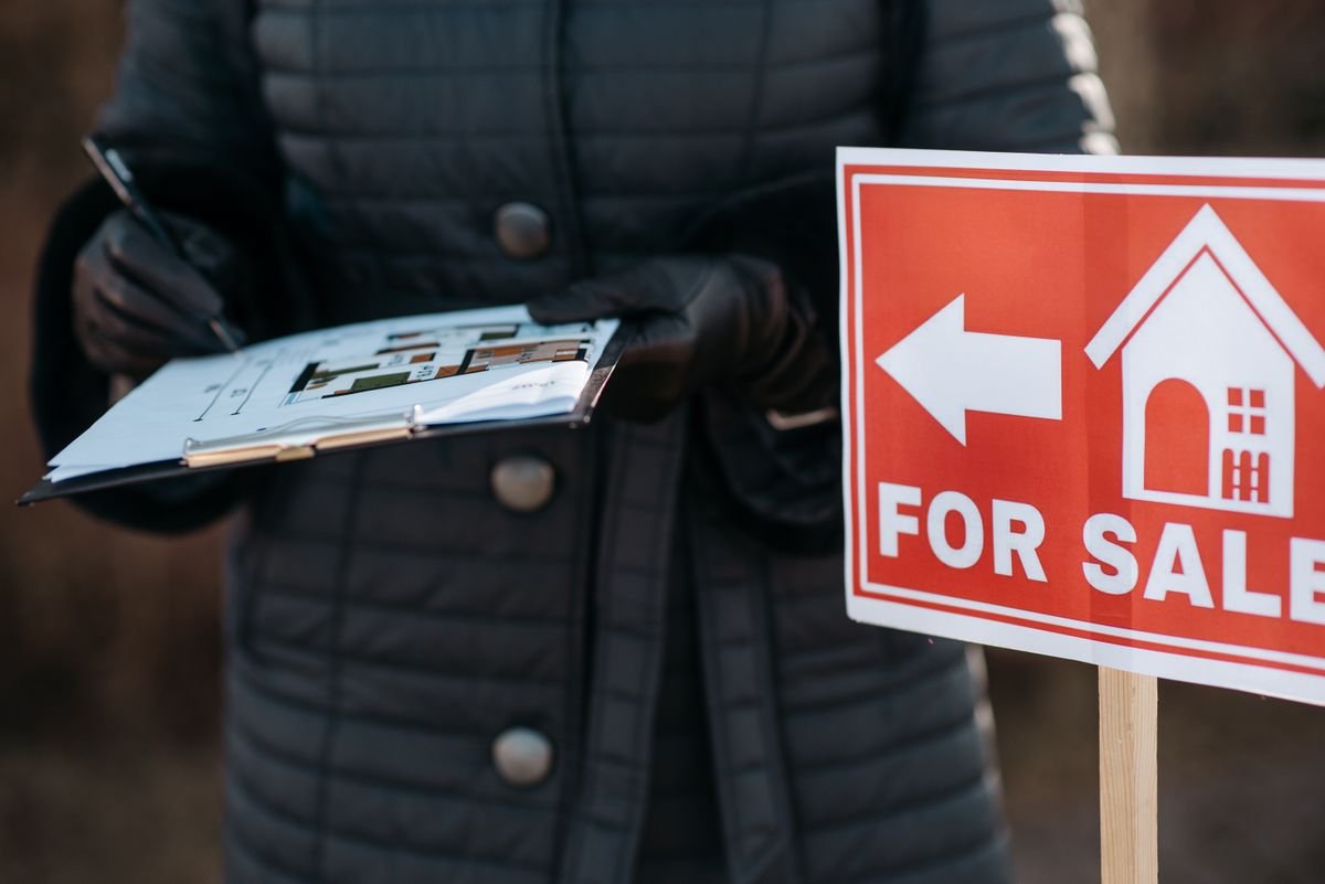 A red For Sale sign beside an estate agent holding a clipboard