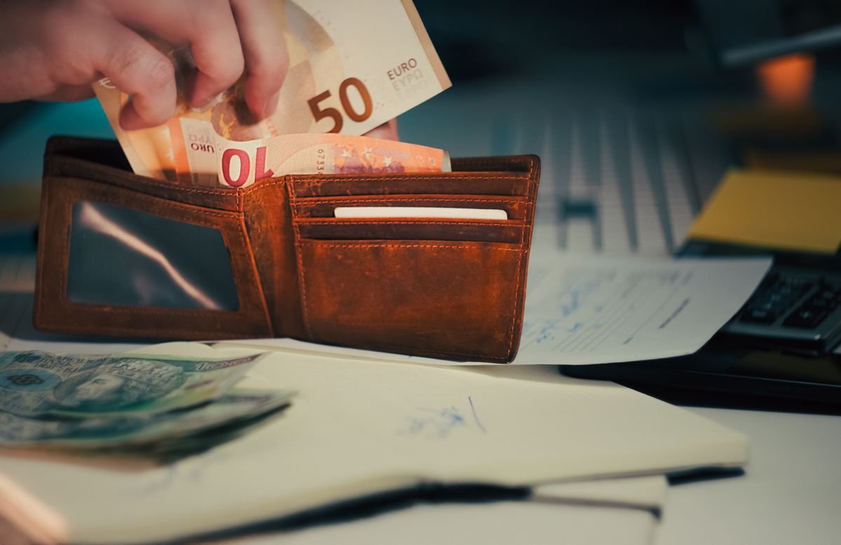 A leather wallet with euro banknotes beside paperwork and a calculator