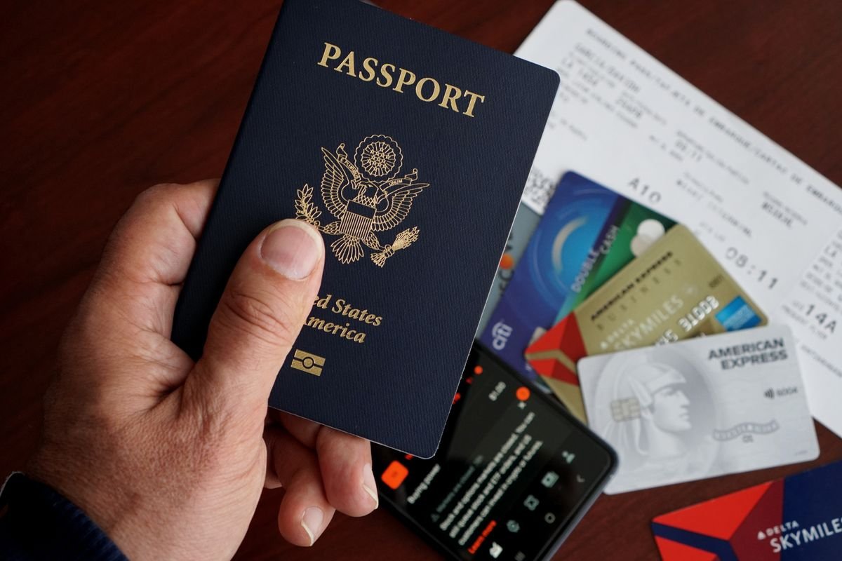 A hand holding a United States passport with a boarding pass and cards