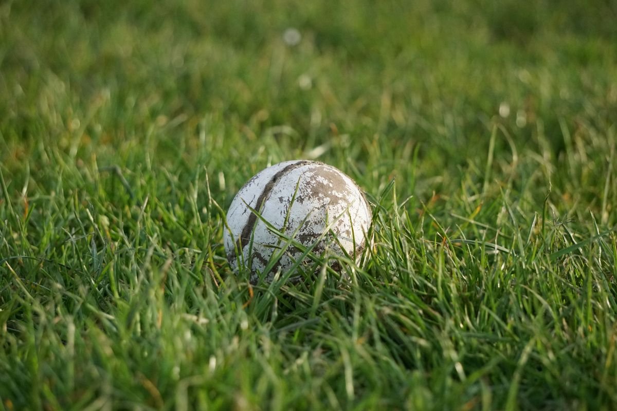 A weathered sliotar resting in the grass on a pitch