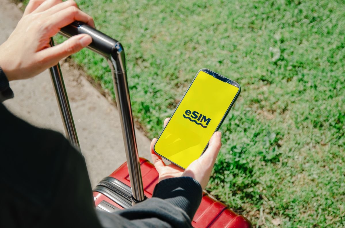 A traveler holding a phone with an eSIM on screen beside a suitcase