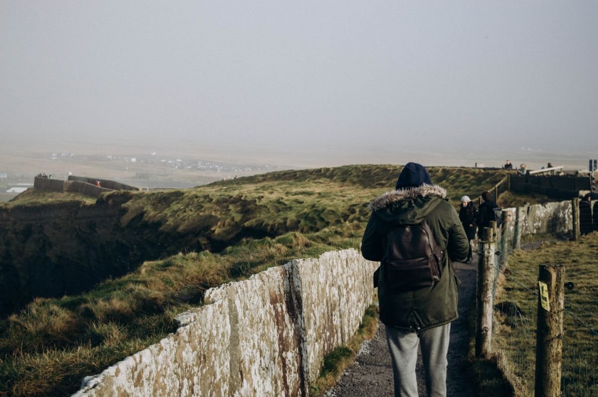 A walker on the cliff path with the fence on the inside, the safe side to stay.