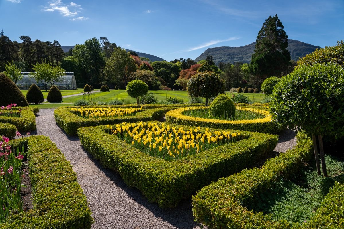 Formal estate garden with clipped hedges and spring flowers, mountains behind
