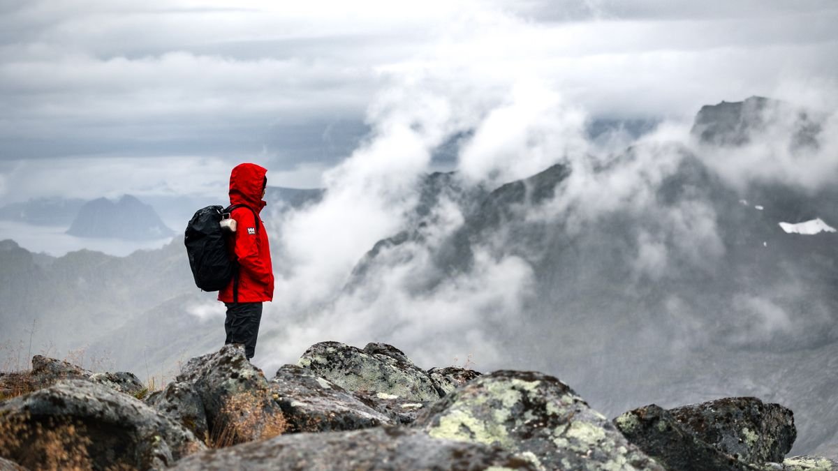 A hiker in a red waterproof shell jacket above misty winter mountains