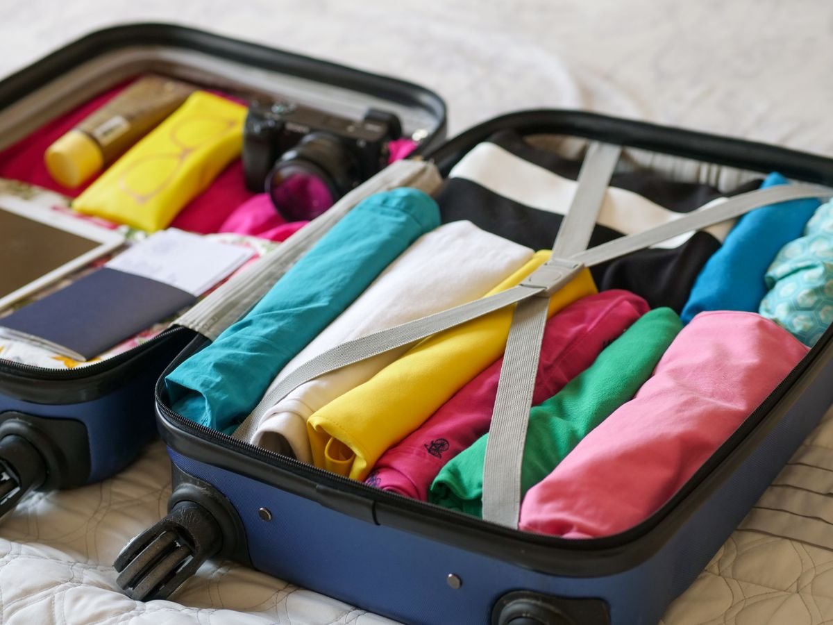An open suitcase packed with folded clothes on a bed