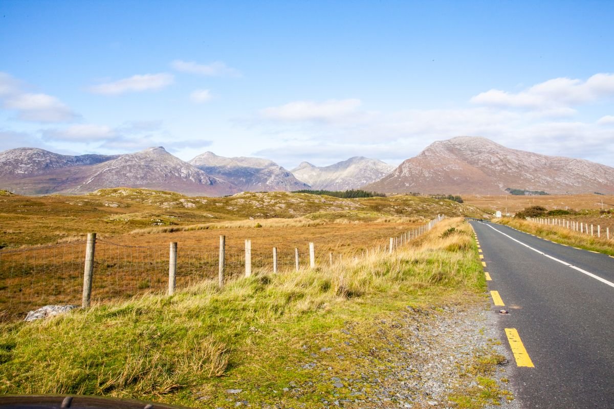 Empty narrow road through open Irish countryside with mountains in the distance