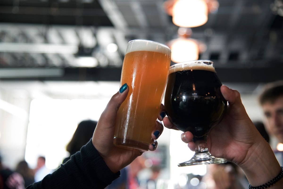 Two hands clinking a pale ale and a dark stout in a toast inside a pub