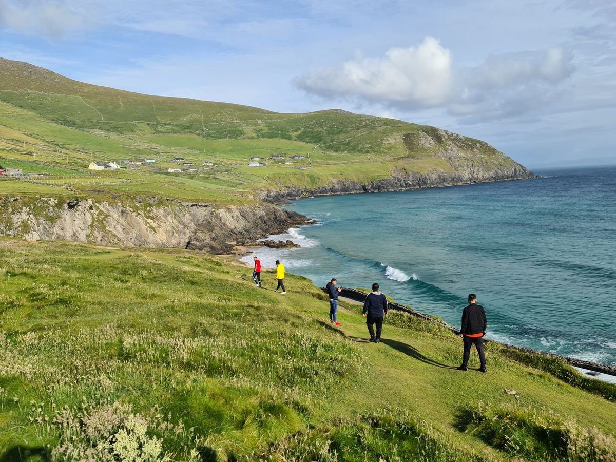 People walking a green coastal trail above a bay in Ireland