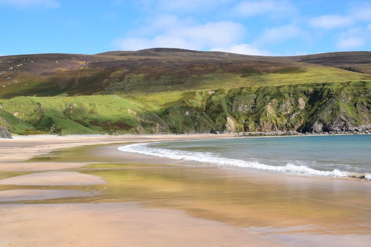 Secluded sandy cove at Boyeeghter Bay between green headlands in Donegal