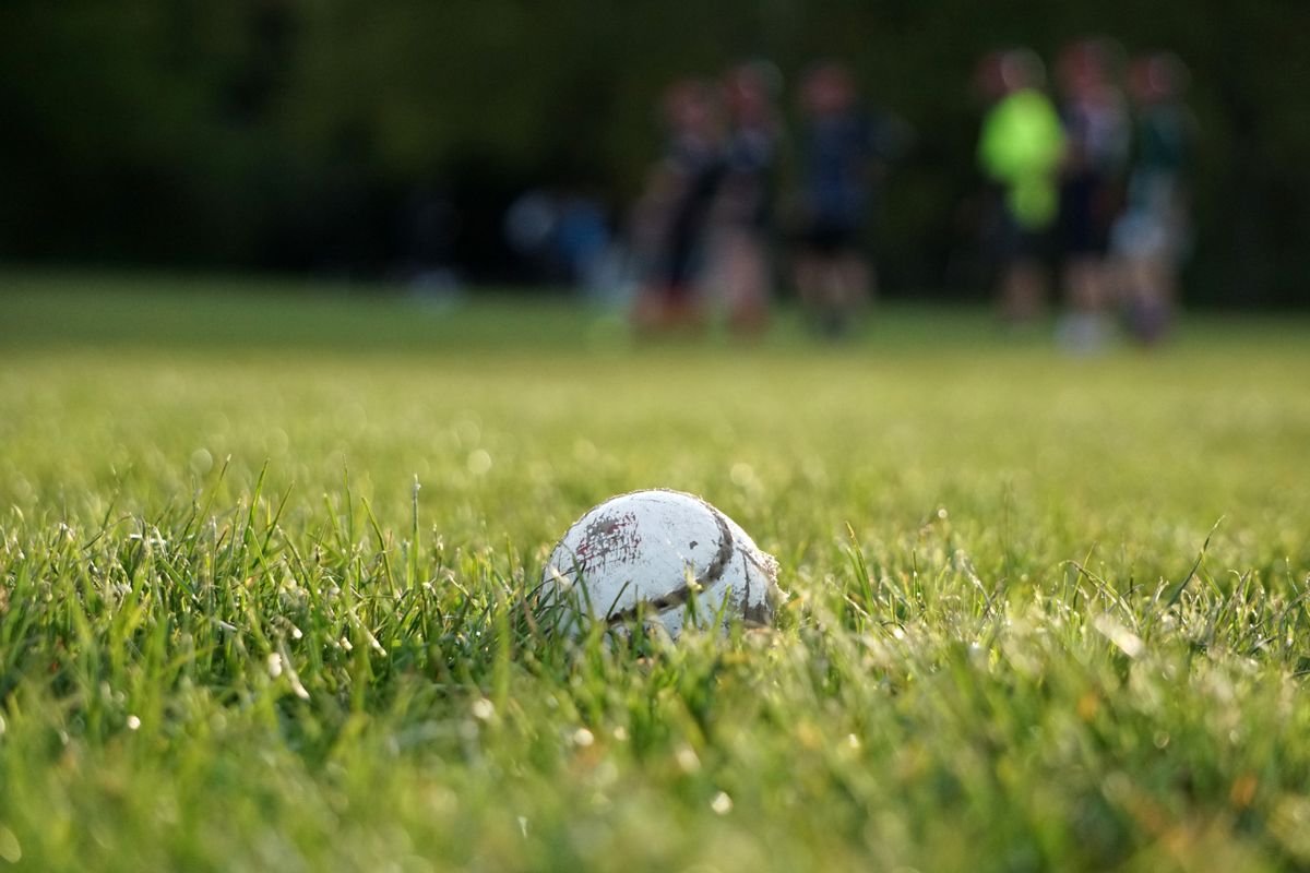 A sliotar on a grass pitch with players in the background during a match