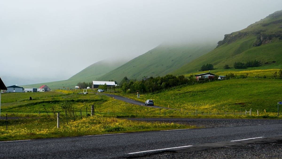 A car on a narrow rural road winding through misty green hills in Ireland