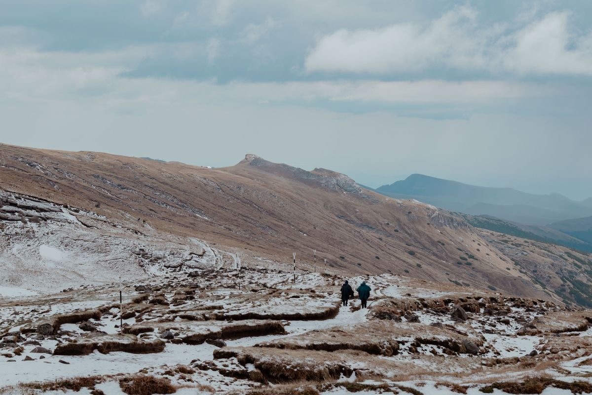 Two walkers on a snow-dusted upland trail under a grey winter sky