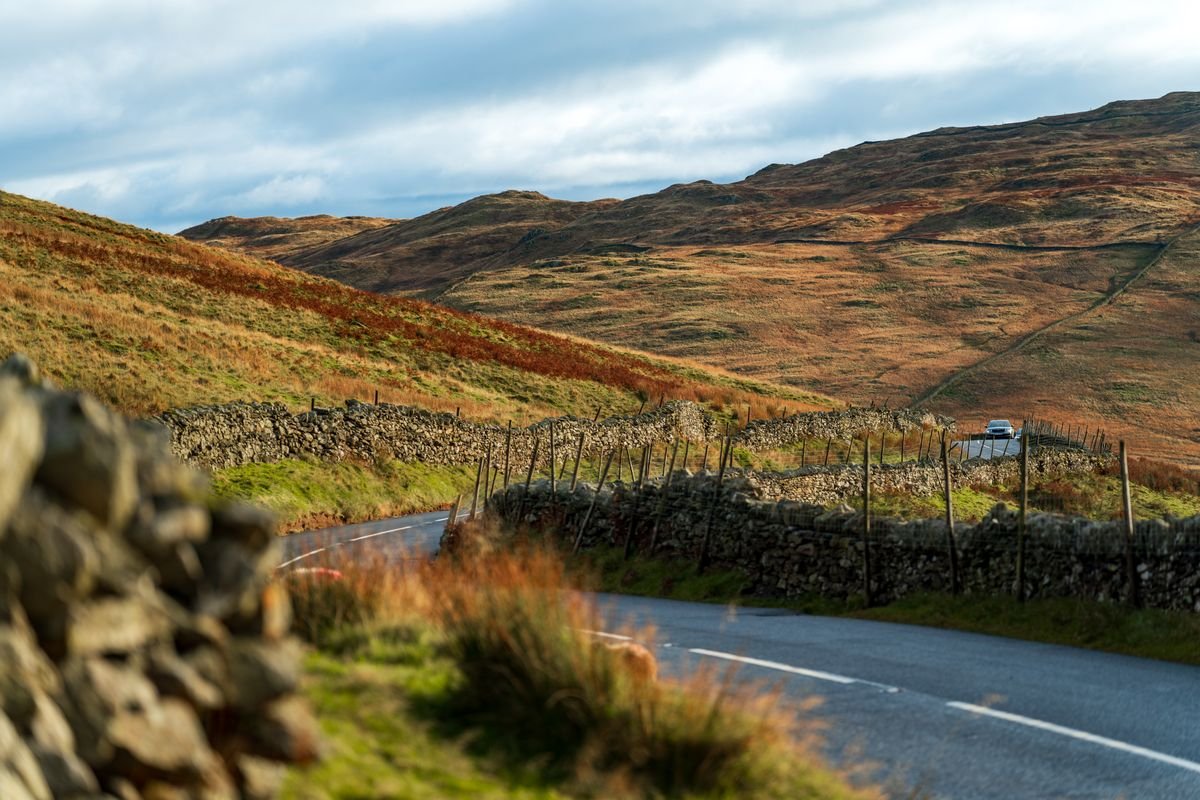 Car on a winding rural road between dry stone walls and hills
