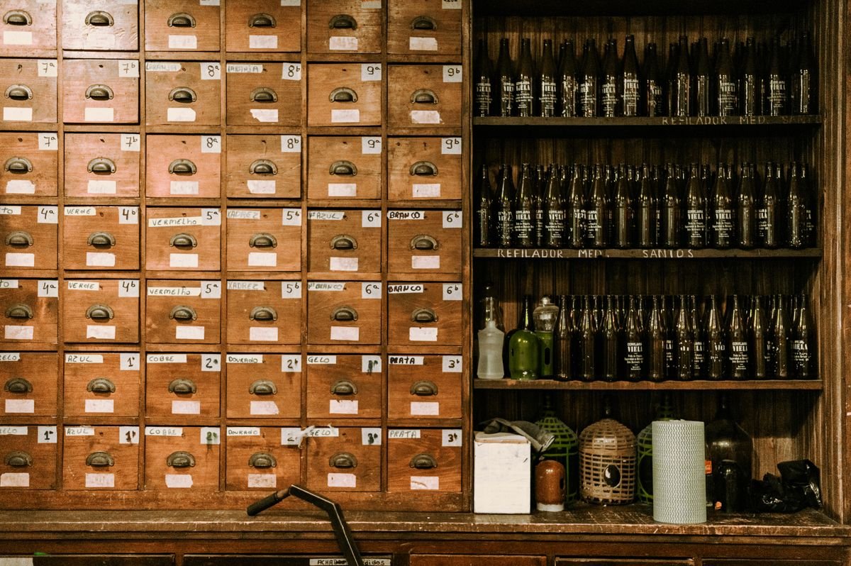 Rows of old bottles on wooden shelves beside a wall of small labeled grocer drawers in a dim traditional pub interior.