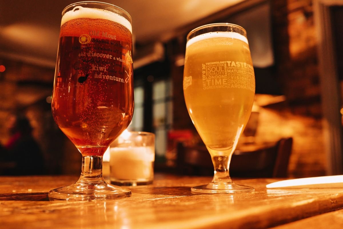 Two beers and a candle on a worn wooden pub table in a warm, low-lit room
