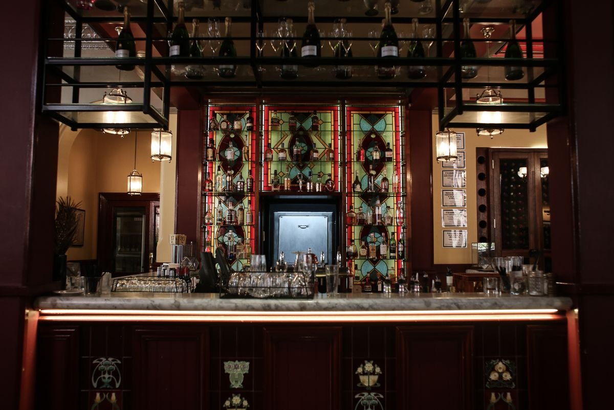 Ornate Victorian pub bar back with stained glass panels, a marble counter and old brass lamps