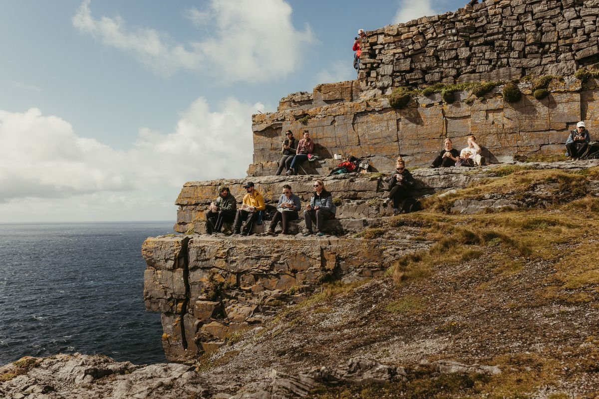 A small group of tourists sitting and exploring the ruins of an Irish cliff fort with the Atlantic visible behind them