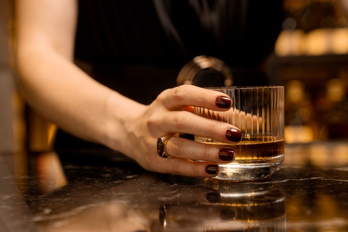 A hand resting on a glass of amber Irish whiskey on a dim pub bar.