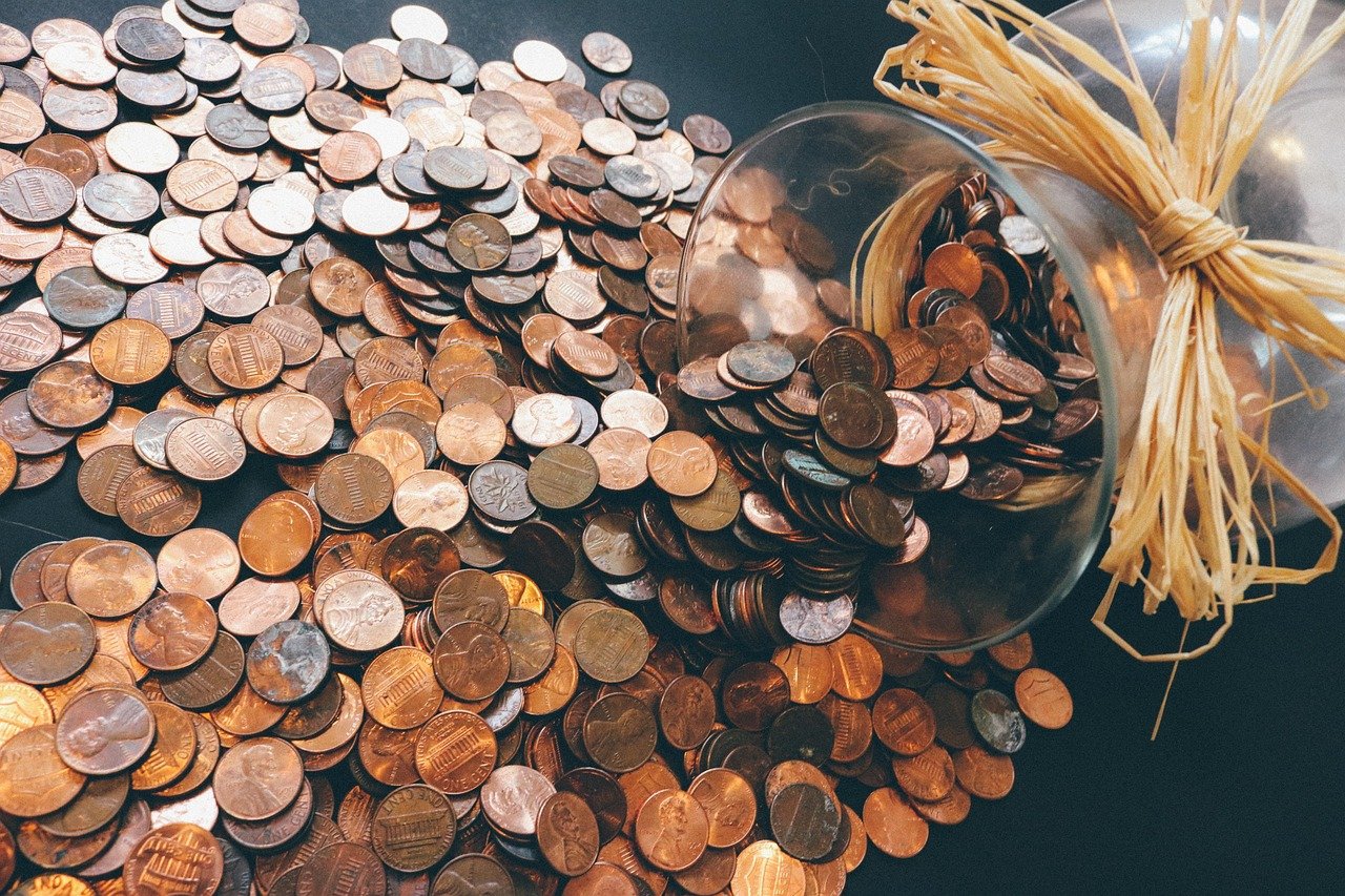 Coins spilling out of a glass jar onto a dark table