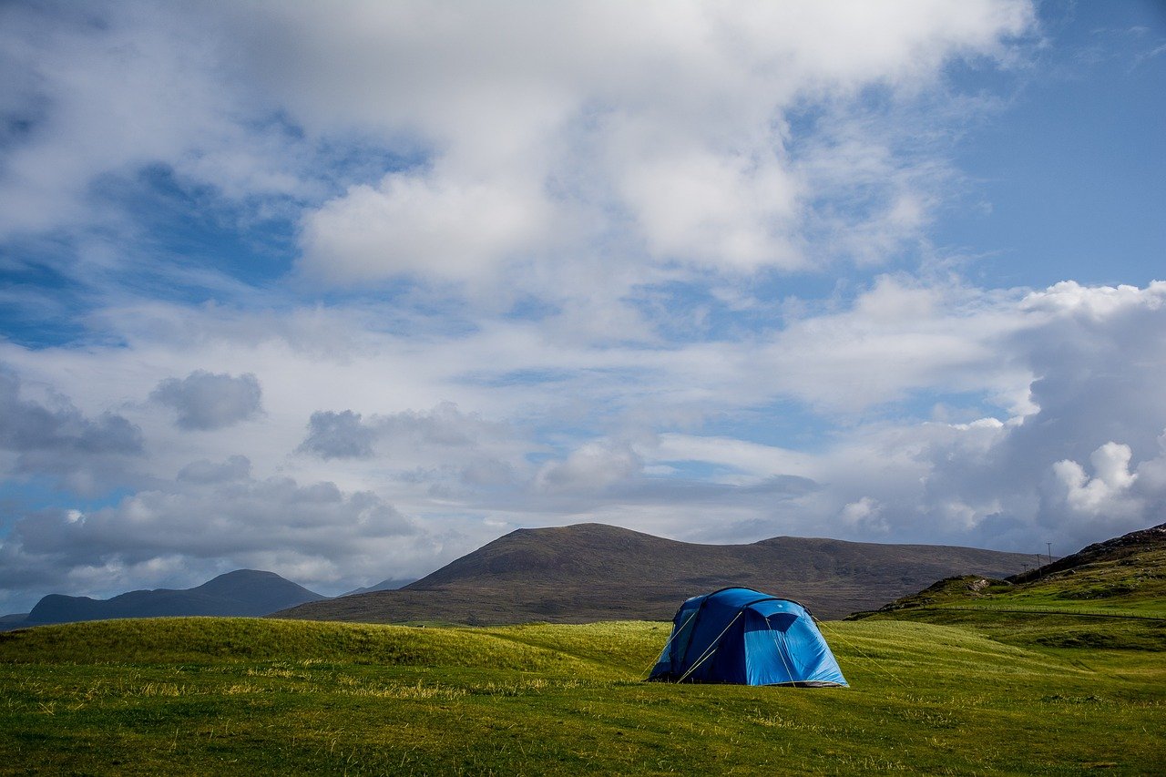 Blue tent pitched in green Irish hills under a cloudy sky