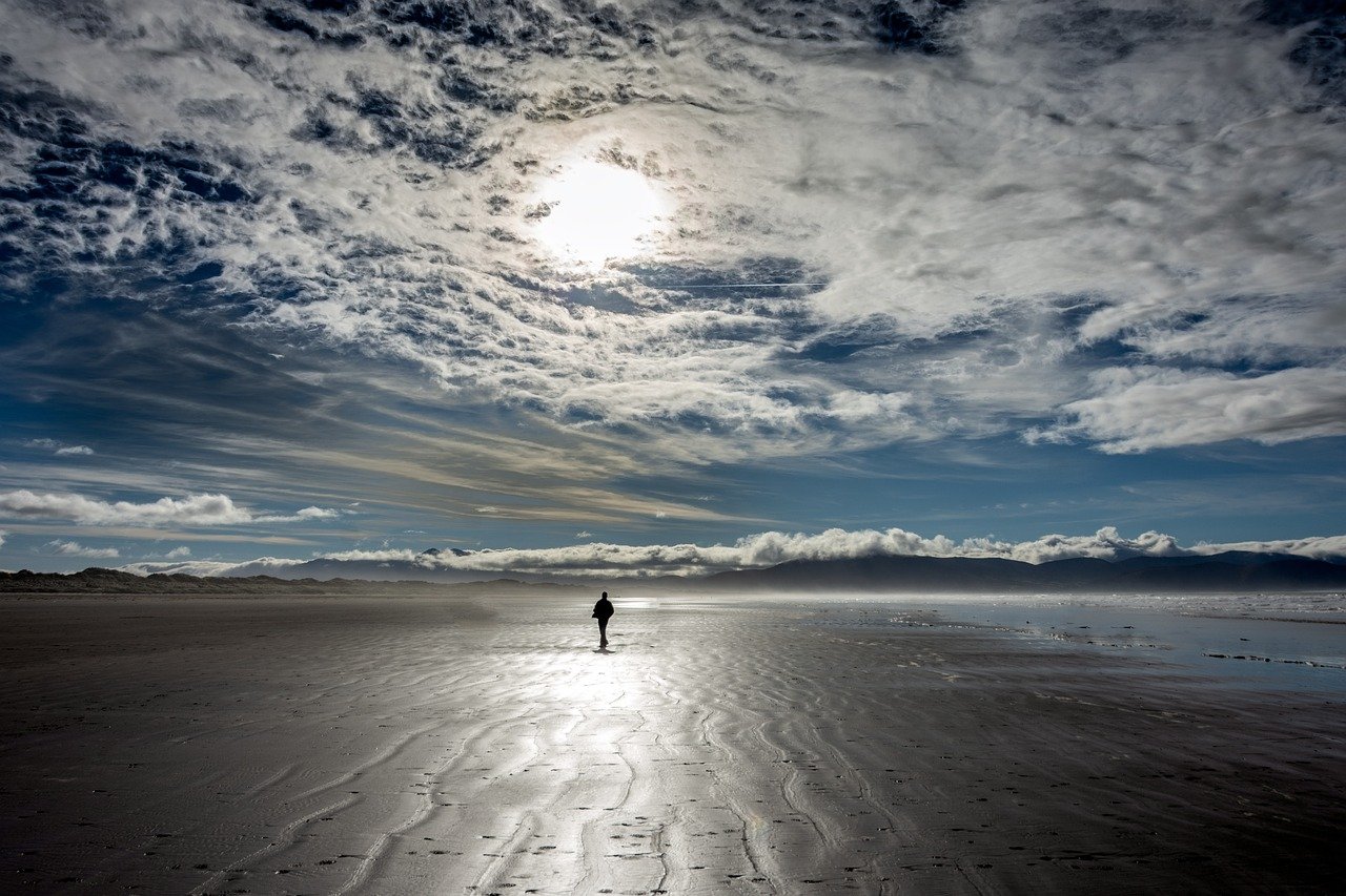 A lone walker on the vast flat sand of Inch Beach reaching into Dingle Bay.